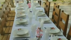 Een lange eettafel, gedekt met witte borden, glazen en bestek, omringd door houten stoelen.