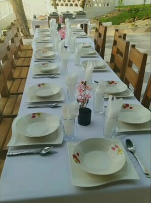 Een lange eettafel, gedekt met witte borden, glazen en bestek, omringd door houten stoelen.