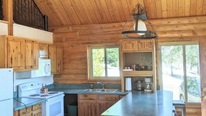 A log cabin kitchen with a central island, wooden cabinets, a stove, and a sink. - Authentic Log Cabin w/ fire pit - 45 Mins to Yellowstone! (Island Park)