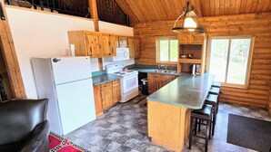 A log cabin kitchen with a refrigerator, stove, microwave, and wooden cabinets. - Authentic Log Cabin w/ fire pit - 45 Mins to Yellowstone! (Island Park)