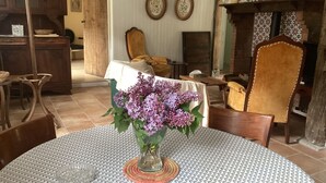 A dining area with a round table covered by a patterned tablecloth, a vase with purple flowers, and a wooden cabinet in the background. - Charming cabin by a lake in the heart of the Landes d'Armagnac forest (Losse)