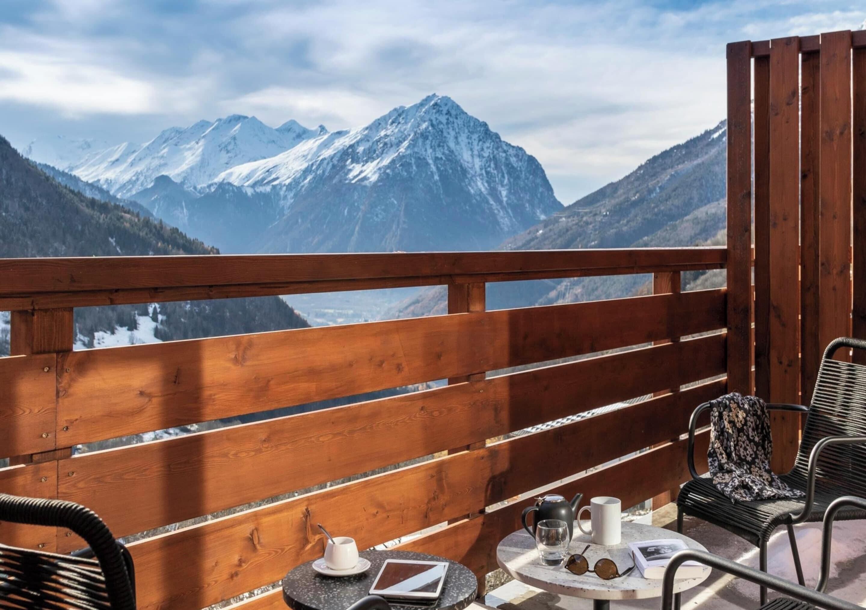 A wooden balcony with a table and chairs, a kettle, a mug, and a glass.