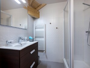 Un baño moderno con tocador de madera, cabina de ducha con mampara de vidrio y pared con azulejos blancos.