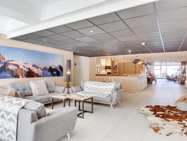 A modern hotel lobby with a large mountain painting, a reception desk, and a cozy seating area with a cowhide rug. - Chalet in Combloux With Mont Blanc Views (Combloux)