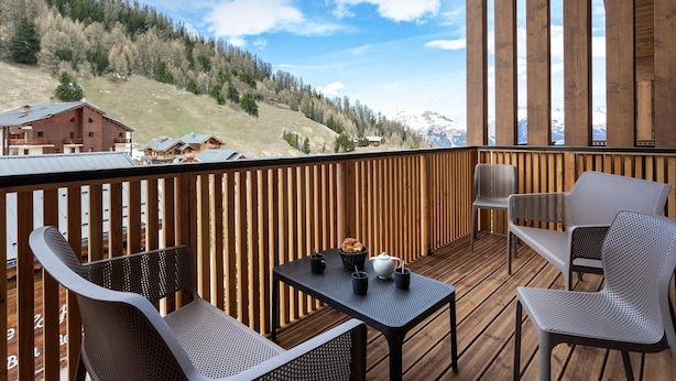 A wooden deck with a table and chairs, overlooking a mountainous landscape with buildings. - Apartment in Plagne 1800 With Ski-in/ski-out (La Plagne-Tarentaise)