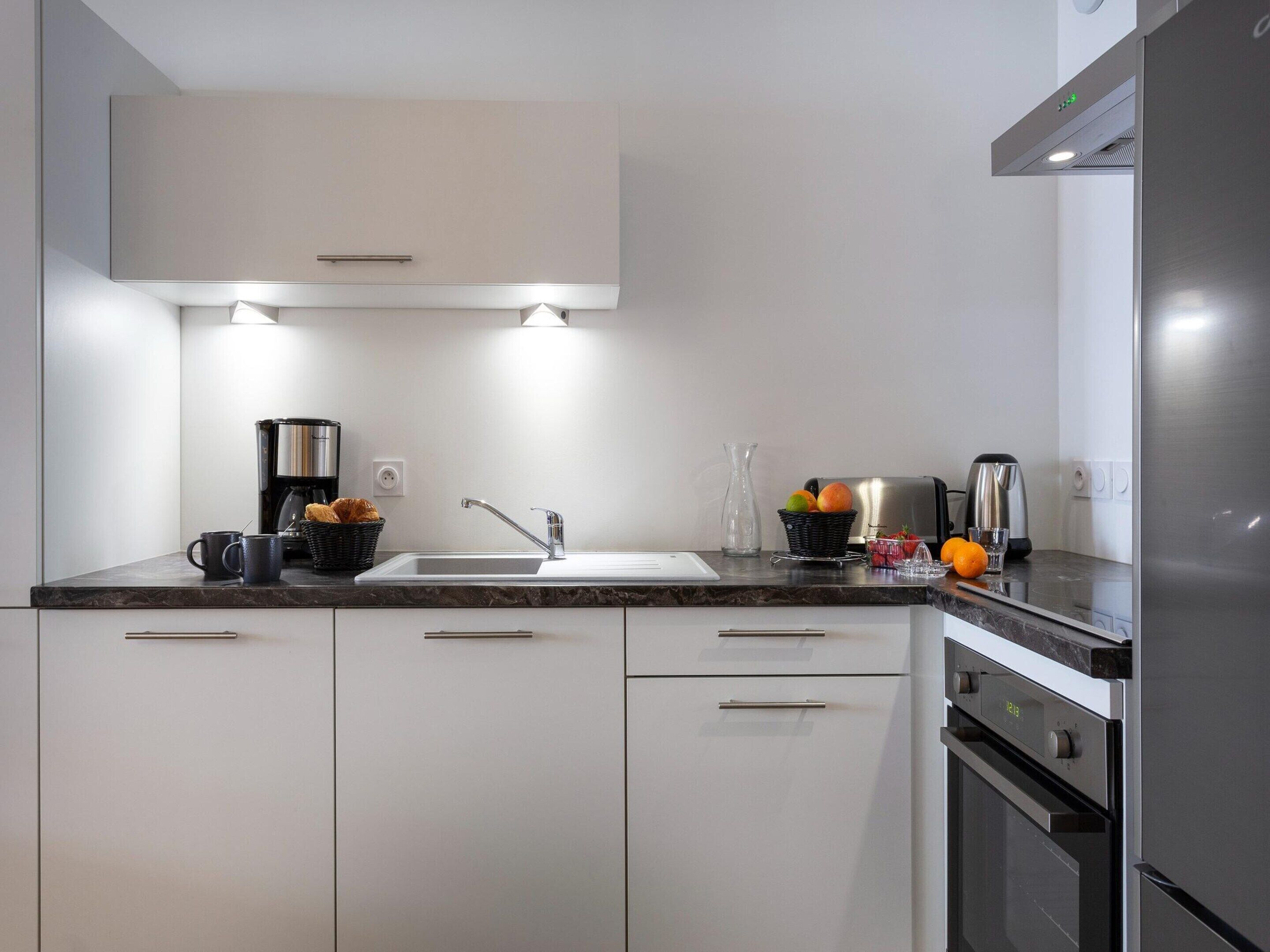 Een moderne keuken met witte kastjes, een roestvrijstalen koelkast, een inbouwoven en een koffiezetapparaat.