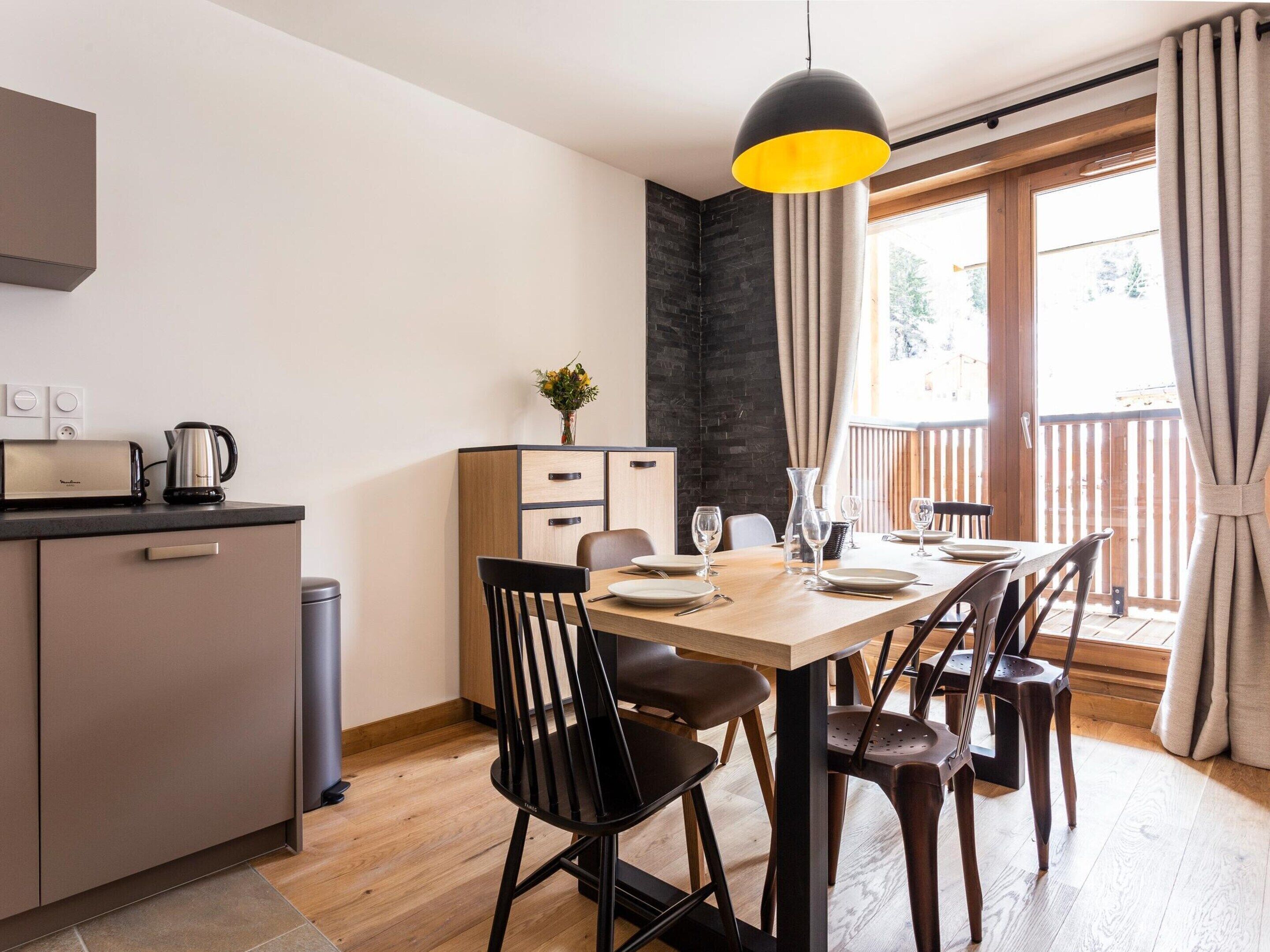 Una cocina moderna con comedor, suelo de madera y un ventanal con cortinas.