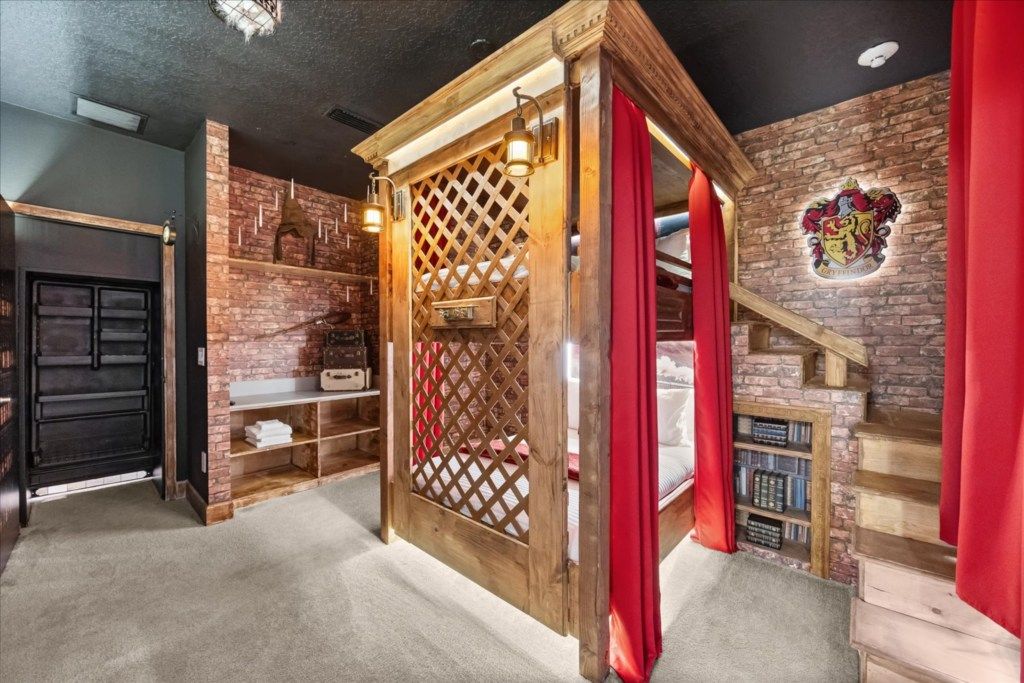 Une pièce avec un lit en bois, un mur en briques, une bibliothèque et un rideau rouge.