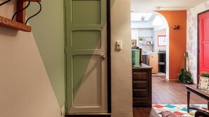 Un pasillo con una puerta verde, una zona de cocina con una puerta roja y una guitarra sobre una mesa.