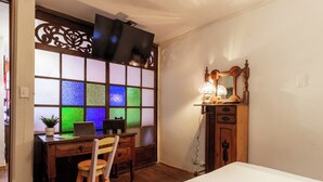 Una habitación con escritorio de madera, una silla, una cama, un aparador con espejo y un televisor montado en la pared.