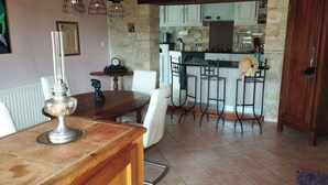 Een eetruimte met een houten tafel en stoelen, een kroonluchter en uitzicht op een keuken met barstoelen.