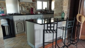 Een keuken met een centraal eiland, twee barkrukken en een raam.