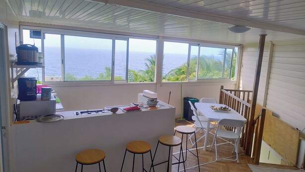 Cozinha com vista para o oceano, área de bar com banquetas e mesa de jantar com cadeiras.