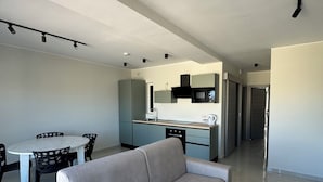 Una sala de estar moderna con un sofá gris, una mesa de comedor con sillas y una cocina con microondas y armarios.
