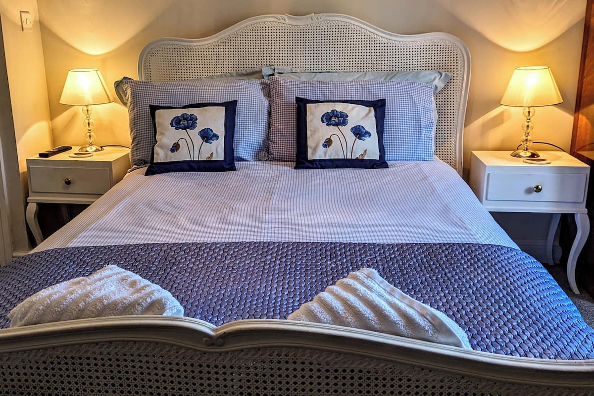 Ein ordentlich bezogenes Bett mit kariertem Überwurf, zwei Kissen mit Blumenmuster und zwei Nachttischlampen.