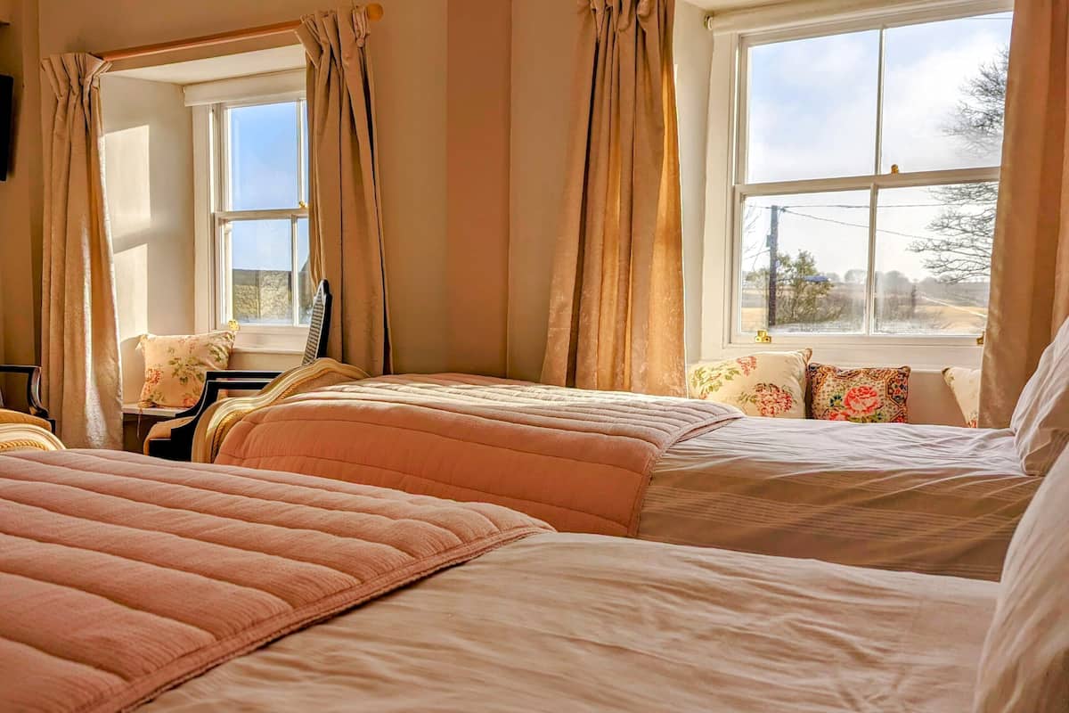 Ein Schlafzimmer mit zwei Betten, einem Fenster mit Vorhängen und Blick ins Freie.