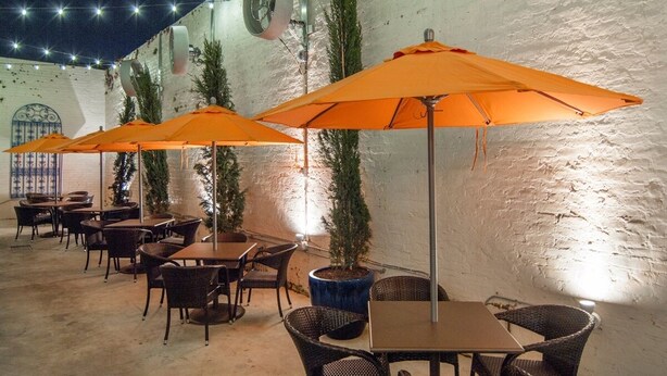 Une terrasse extérieure avec des tables et des chaises, des parasols orange et des plantes en pot.