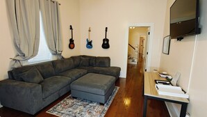 Un salon avec un canapé d’angle, une petite table sur laquelle est posée une télévision à écran plat, et trois guitares accrochées au mur.