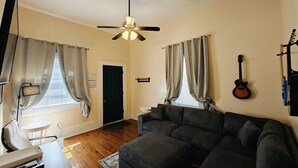 Un salon avec un canapé gris foncé, un ventilateur de plafond et une guitare accrochée au mur.