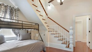 Une chambre avec un lit superposé, un escalier avec des rampes blanches et une porte donnant sur une autre pièce.