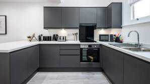 Une cuisine moderne avec des meubles de rangement aux couleurs sombres, un four encastré, un four à micro-ondes et un évier.
