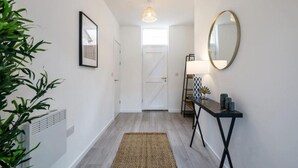Un couloir avec une porte blanche, un miroir, une petite table ornée d’objets décoratifs et une plante.