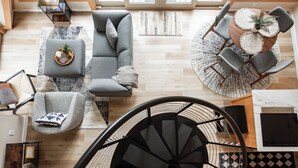 A modern living room with a grey sofa, a round coffee table, and a staircase with a black railing. - Riverfront A-Frame Cabin in the Mountains w/ Sauna & Private Hiking Trail (Ellijay)