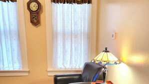 A living room with a black leather sofa, a matching ottoman, a vintage clock on the wall, and a lamp on a side table. - 3bdr Apartment in Museum Hill - #3 (Saint Joseph)