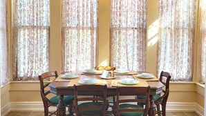 A dining room with a table set for four, surrounded by four chairs with green cushions, and a chandelier above. - 3bdr Apartment in Museum Hill - #3 (Saint Joseph)