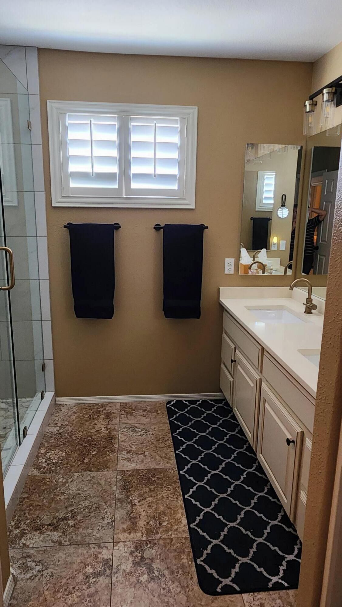 A bathroom with two towels hanging on the wall, a shower, a sink with a mirror, and a patterned rug on the floor.