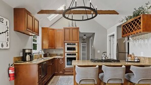 Una cocina con armarios de madera, una isla central con taburetes de bar, una lámpara de araña y un reloj en la pared.