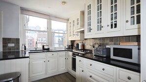 A modern kitchen with white cabinets, a black countertop, and a window providing a view of buildings outside. - Large 3 bedroom apartment in Heart of Theatre District (London)