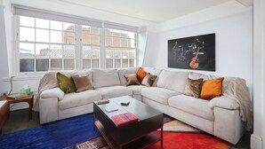 A modern living room with a white sofa, a coffee table, and a large window. - Large 3 bedroom apartment in Heart of Theatre District (London)