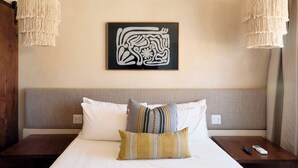 Een hotelkamer met een bed, twee nachtkastjes, een aan de muur bevestigd kunstwerk en twee hangende lampen.