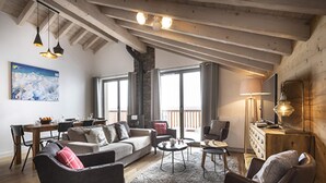 A spacious living area with a high ceiling, a sofa, chairs, a coffee table, and a fireplace. - Cozy Apartment in La Rosiere With ski Access (Montvalezan)