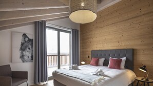 A bedroom with a large bed, a chair, a painting of a wolf, and a balcony with a railing. - Cozy Apartment in La Rosiere With ski Access (Montvalezan)