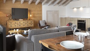A modern living room with a wooden ceiling, a television, a sofa, and a dining table with plates and glasses. - Cozy Apartment in La Rosiere With ski Access (Montvalezan)