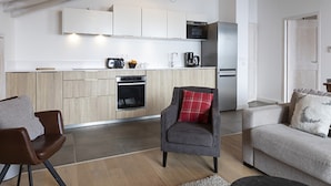 A modern kitchen with wooden cabinets, a microwave, and a refrigerator. There is a gray armchair with a red pillow and a gray sofa with patterned cushions. - Cozy Apartment in La Rosiere With ski Access (Montvalezan)