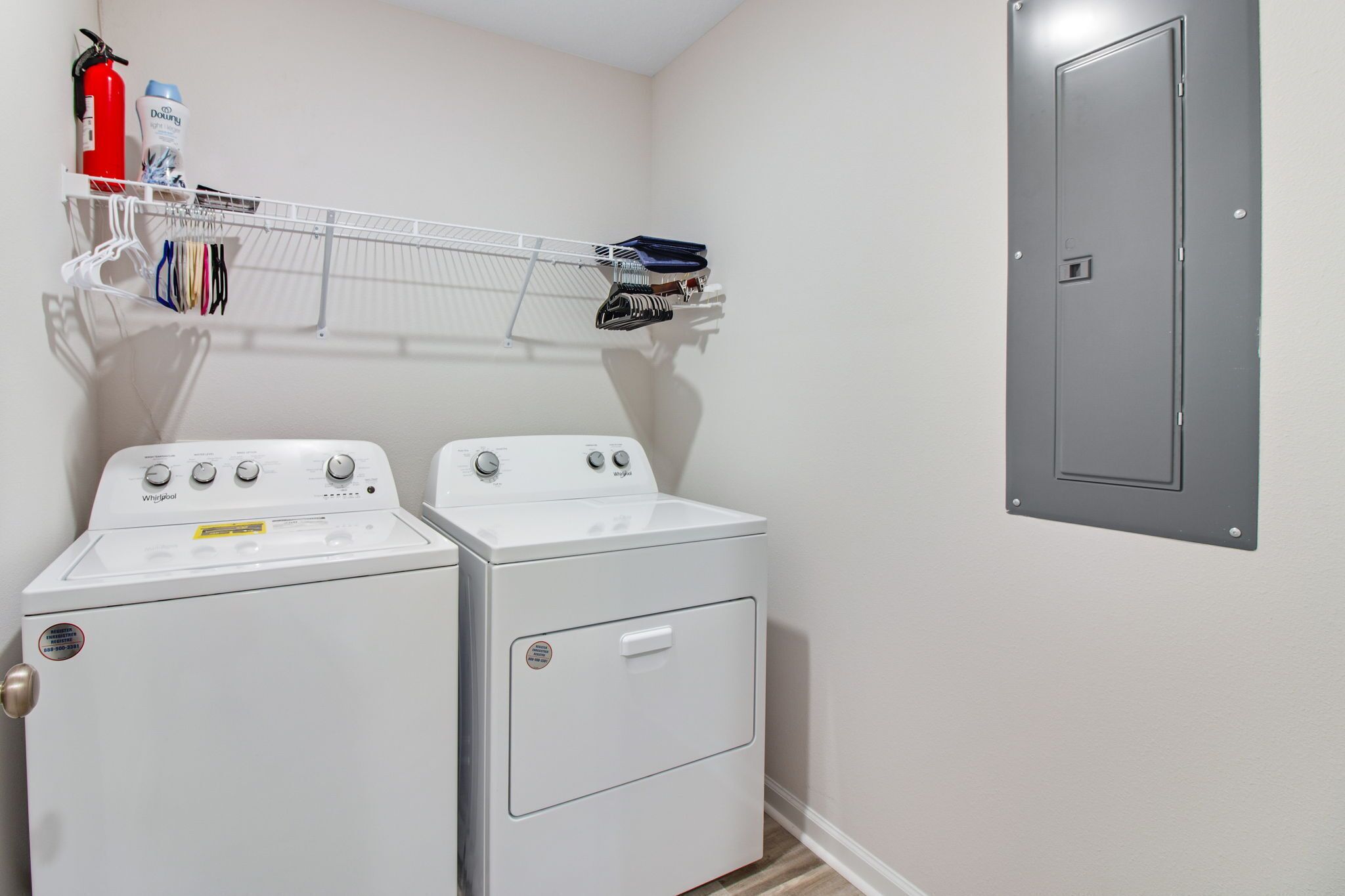 A laundry room with two white Whirlpool washers and dryers, a metal shelf with laundry supplies, and a gray door.