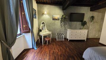 Un dormitorio con piso de madera, tocador blanco, espejo, planta colgante y televisor montado en la pared.