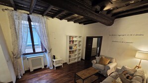 A cozy living room with a wooden floor, a sofa, a coffee table, a bookshelf, and a window with curtains. - "Vicolo del Borgo" ..in the center live the magic of the Middle Ages. (Viterbo)