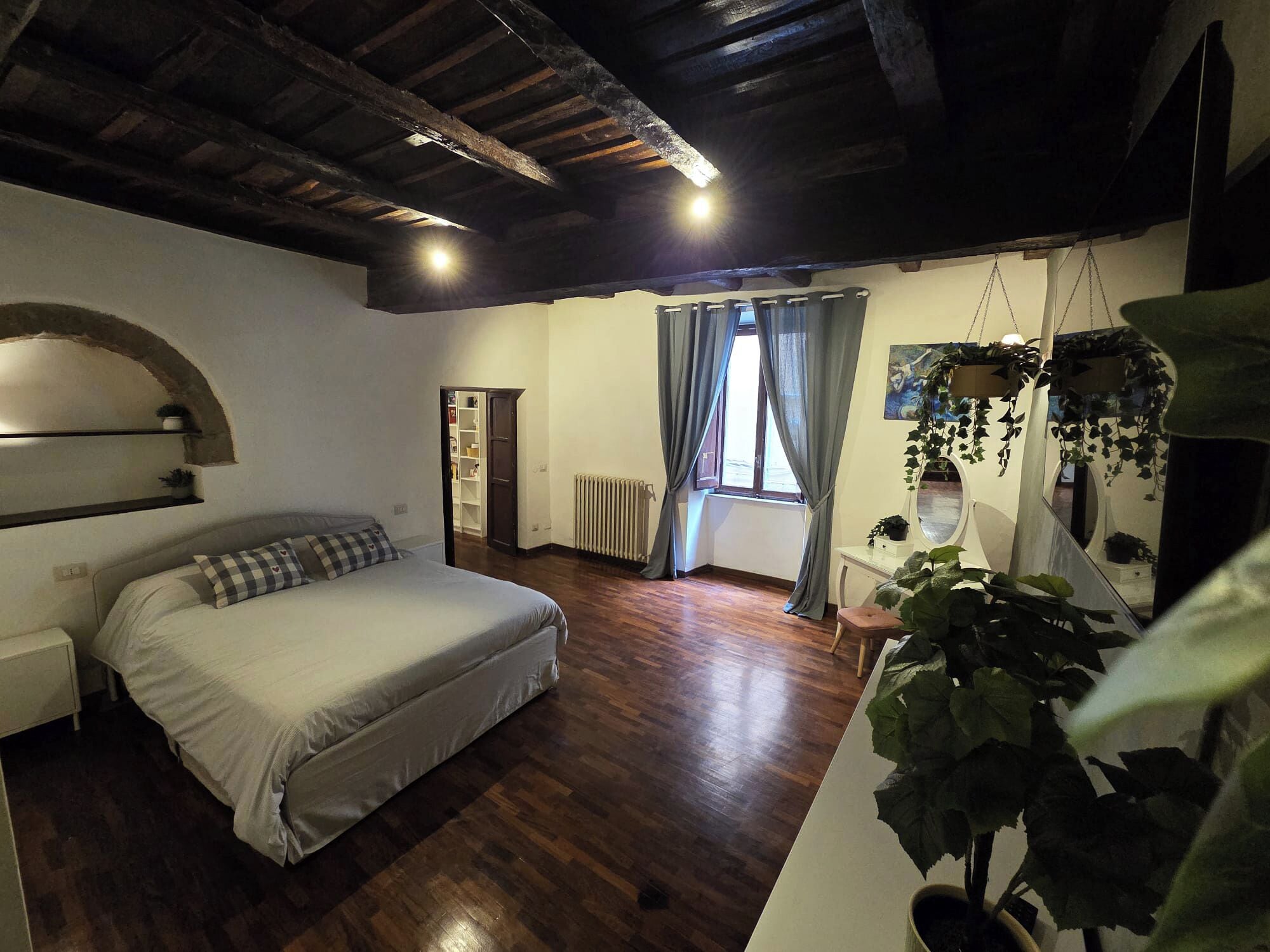 Un dormitorio con cama, suelo de madera, radiador, armario y ventana con cortinas.