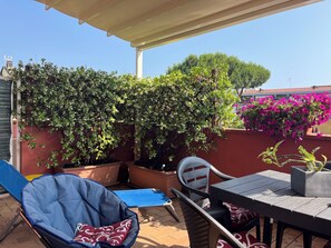 A covered patio with a table and chairs, a blue lounge chair, and potted plants. - One step from the sea in Marina di Carrara (Marina di Carrara)