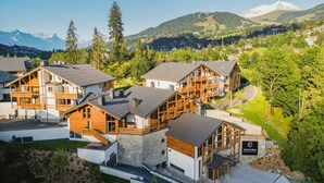 Una moderna struttura ricettiva con diverse cabine in legno, pareti in pietra e vista sulle montagne.