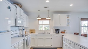 A modern kitchen with white cabinets, a central island, a built-in oven, and a dishwasher.
