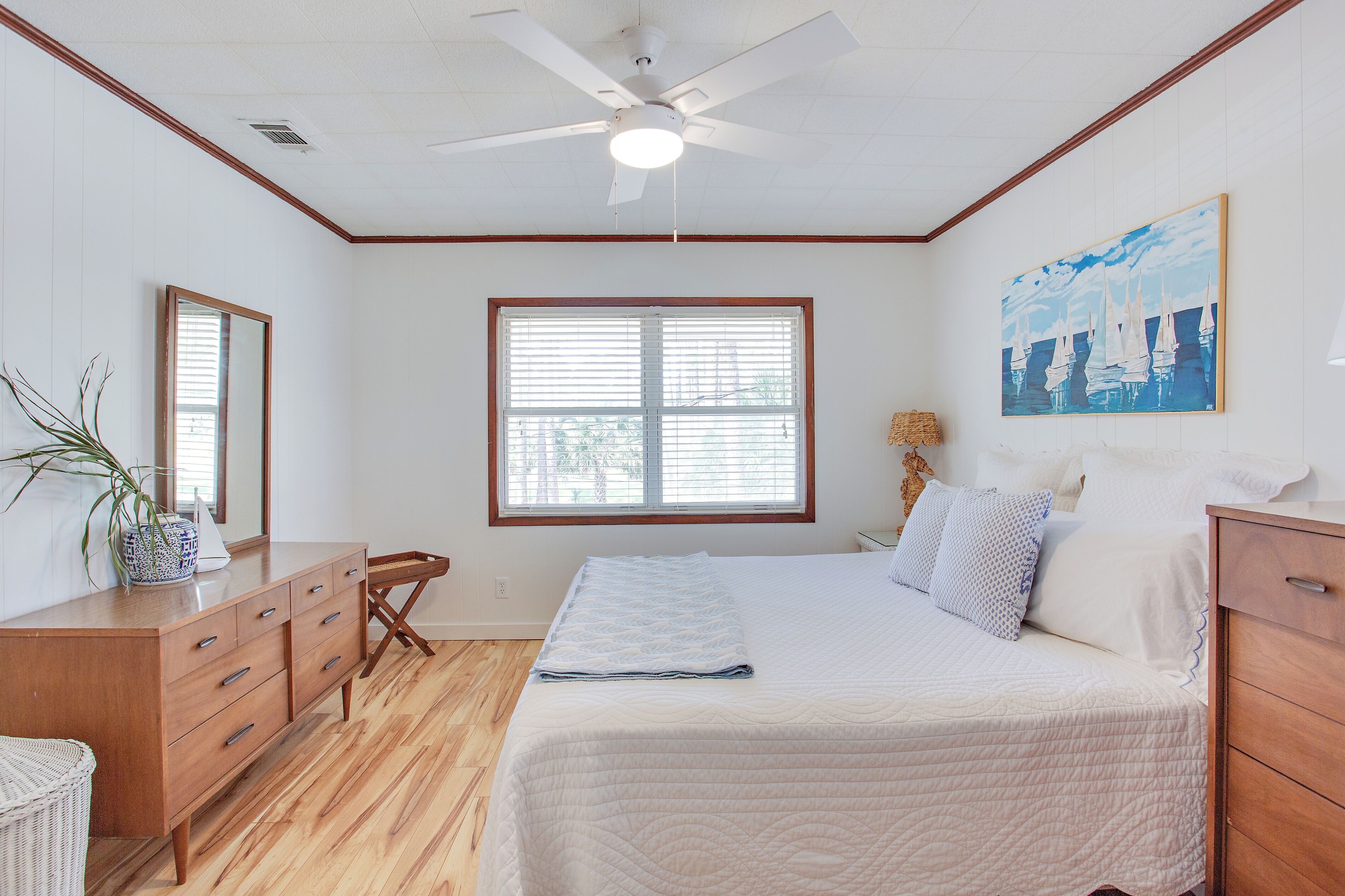 A bedroom with a bed, wooden dresser, and a ceiling fan.