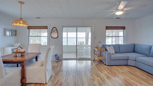 A spacious living room with a wooden floor, a blue sectional sofa, a dining table with chairs, and a ceiling fan.