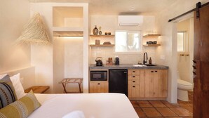 Une chambre d’hôtel compacte comprenant un coin cuisine, un lit avec des oreillers, une petite table et un luminaire suspendu.