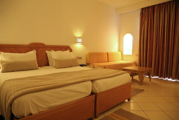 A hotel room with a large bed, a small sofa, a nightstand, and a window with curtains.