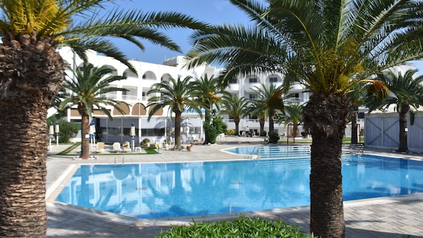 A swimming pool surrounded by palm trees and a building with multiple balconies. - Golf Residence- Family Only (Port El Kantaoui)